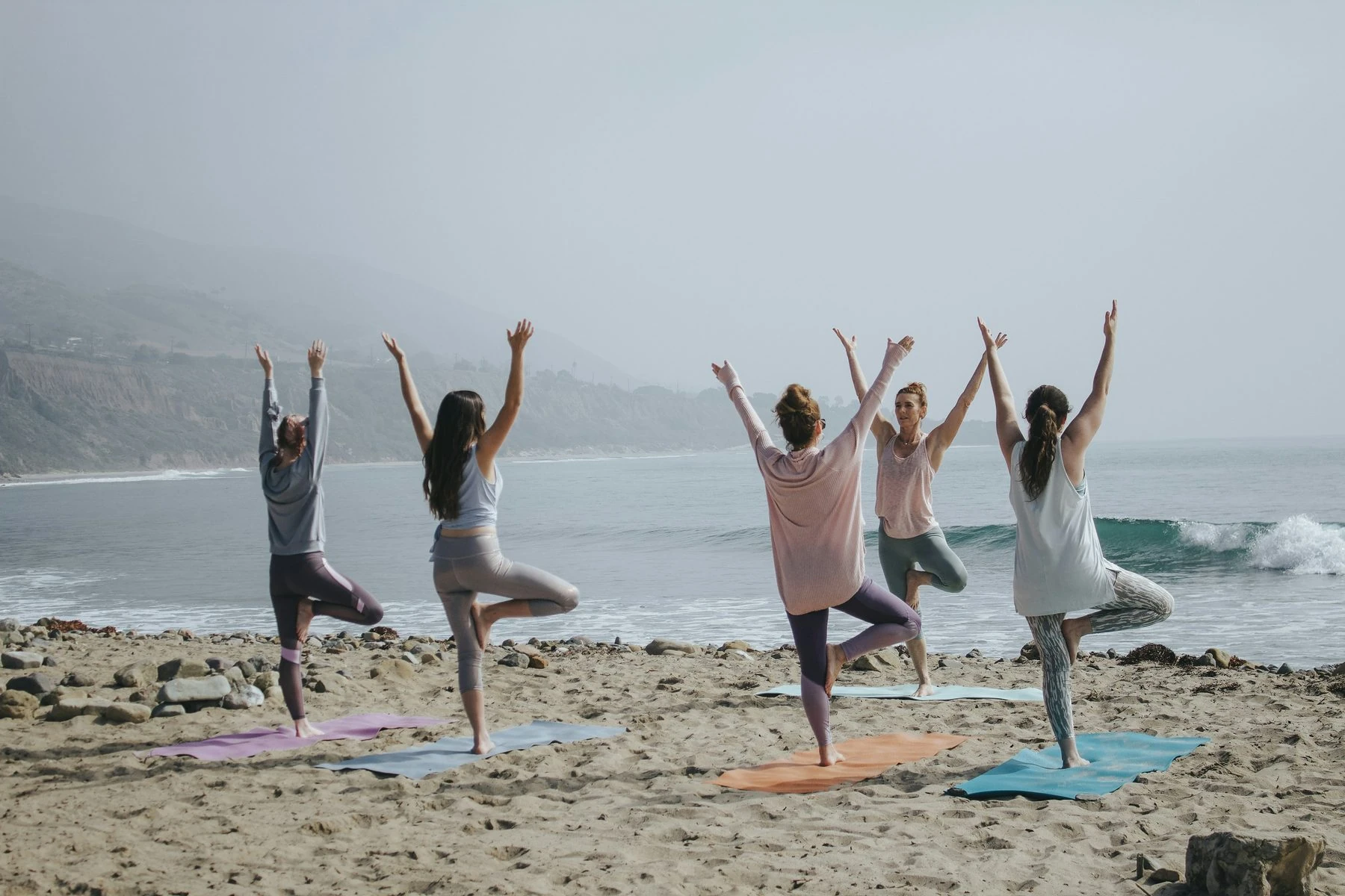 Yoga practitioners on a beach at sunrise, arms raised in celebration